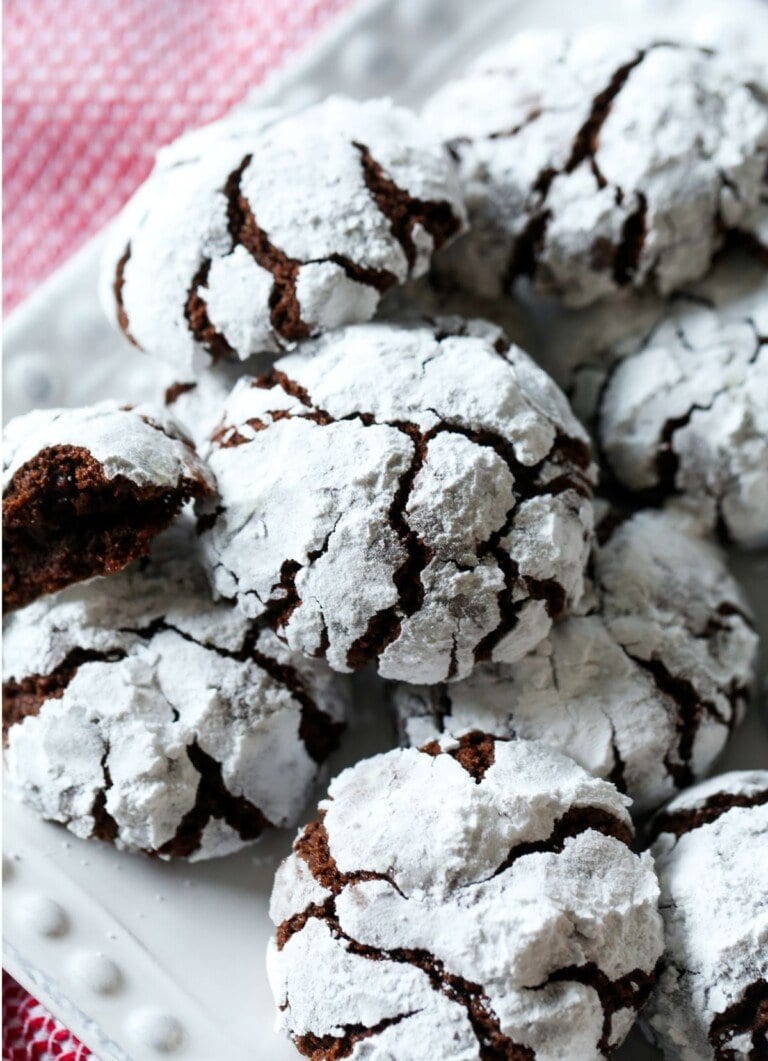 Galletas arrugadas de chocolate recién horneadas sobre un paño de cocina blanco y un mantel de algodón a cuadros. Una de las galletas se ha partido por la mitad para revelar el interior suave.