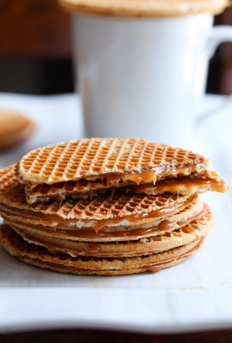 Stroopwafels apilados en un plato junto a una taza de café, con la galleta superior partida por la mitad.