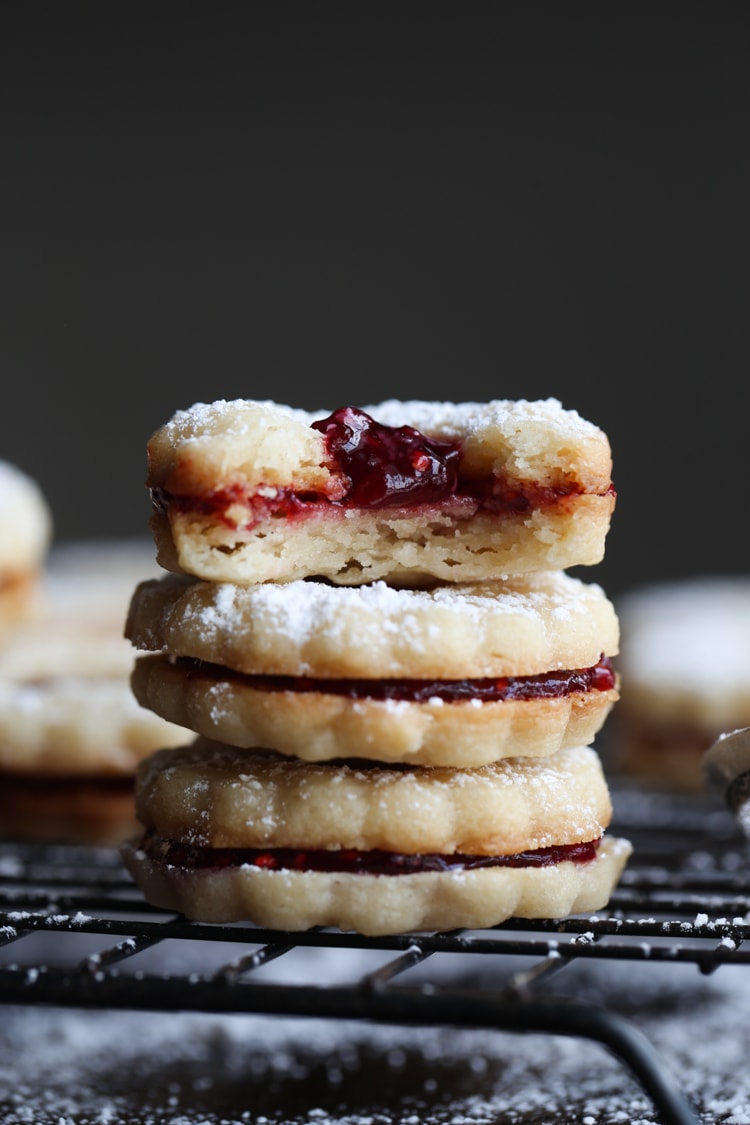 Una pila de galletas Linzer relleno de mermelada de frambuesa sobre una rejilla.