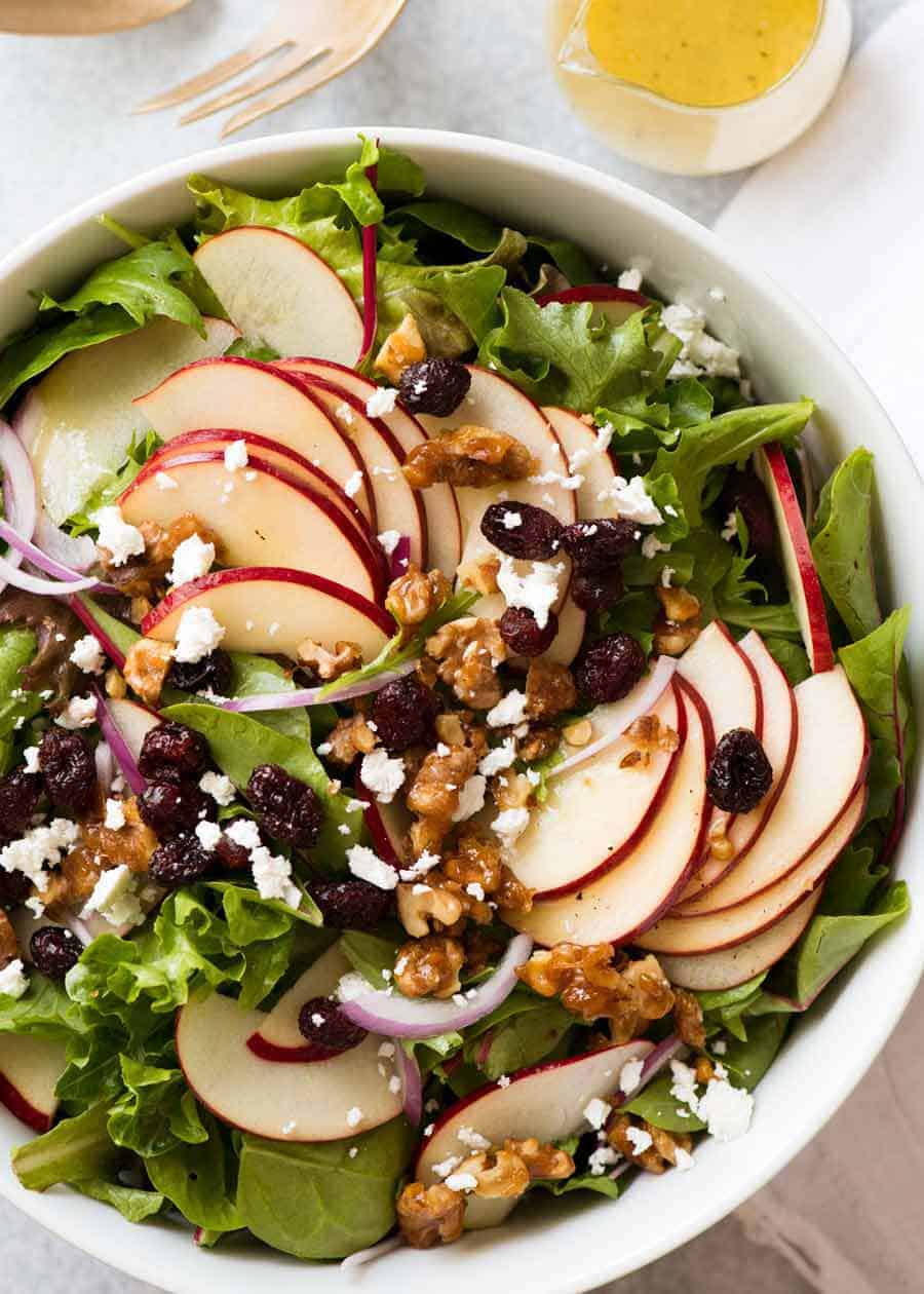 Fotografía aérea de ensalada de manzana con nueces confitadas y arándanos con aderezo de vinagreta al costado