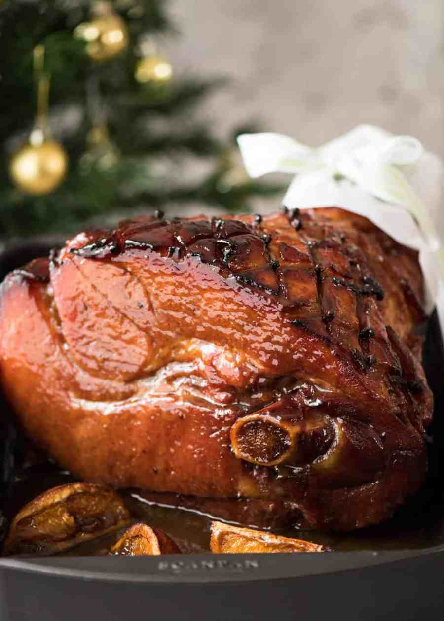 Un jamón horneado reluciente con un glaseado de azúcar moreno de arce en un plato blanco grande.