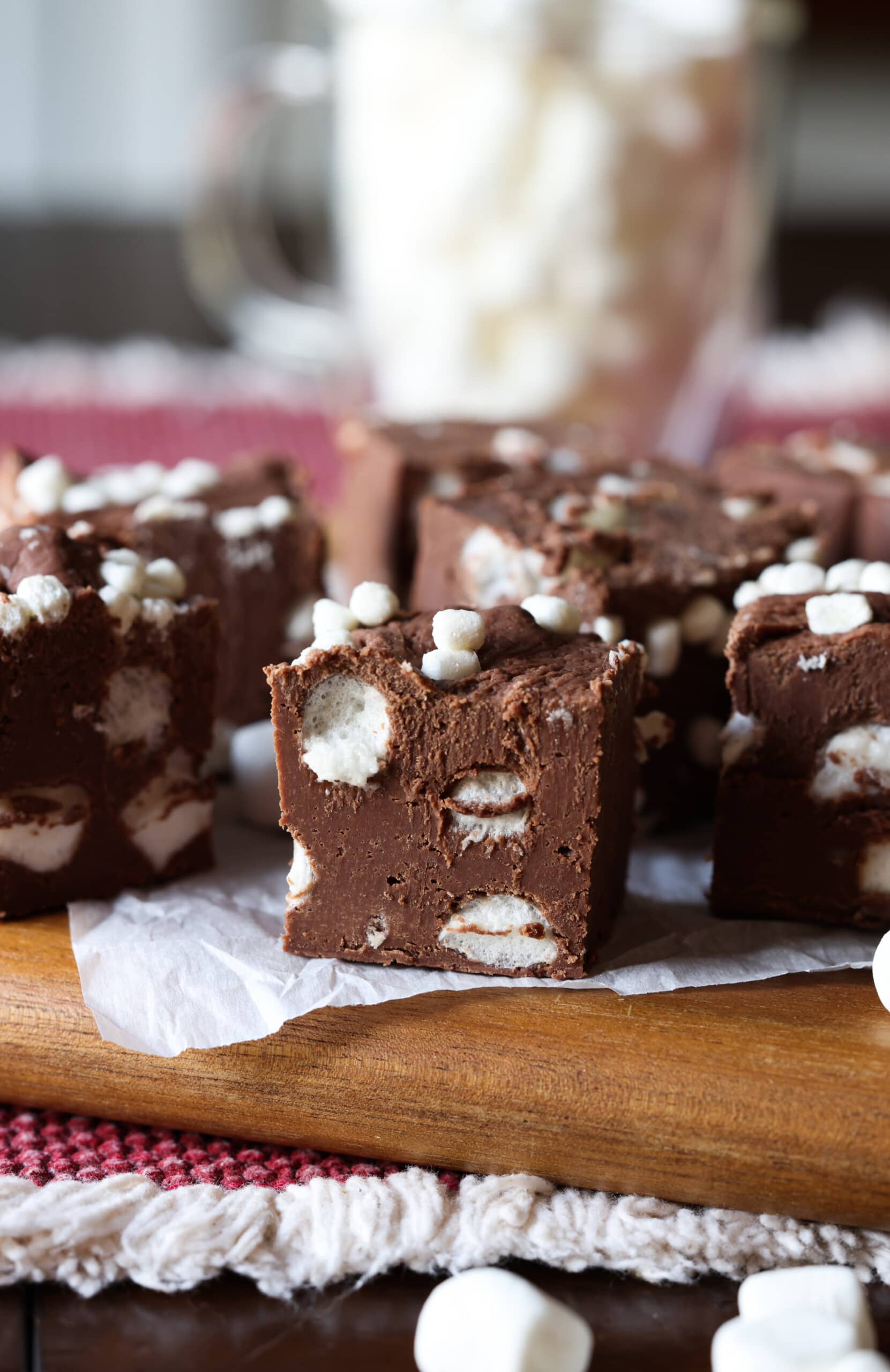 ¡Esta receta fácil de dulce de chocolate caliente combina dos favoritos de invierno en un postre! Fudge cremoso con mini malvaviscos, ¡esta receta es perfecta para regalar en las fiestas! Fudge de chocolate caliente cortado en trozos sobre una tabla para cortar
