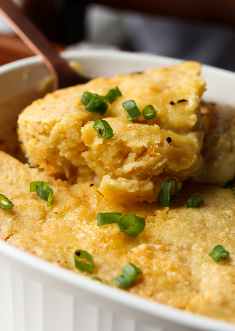 Una cuchara saca una porción de cazuela de pollo con pan de maíz de una fuente para hornear.