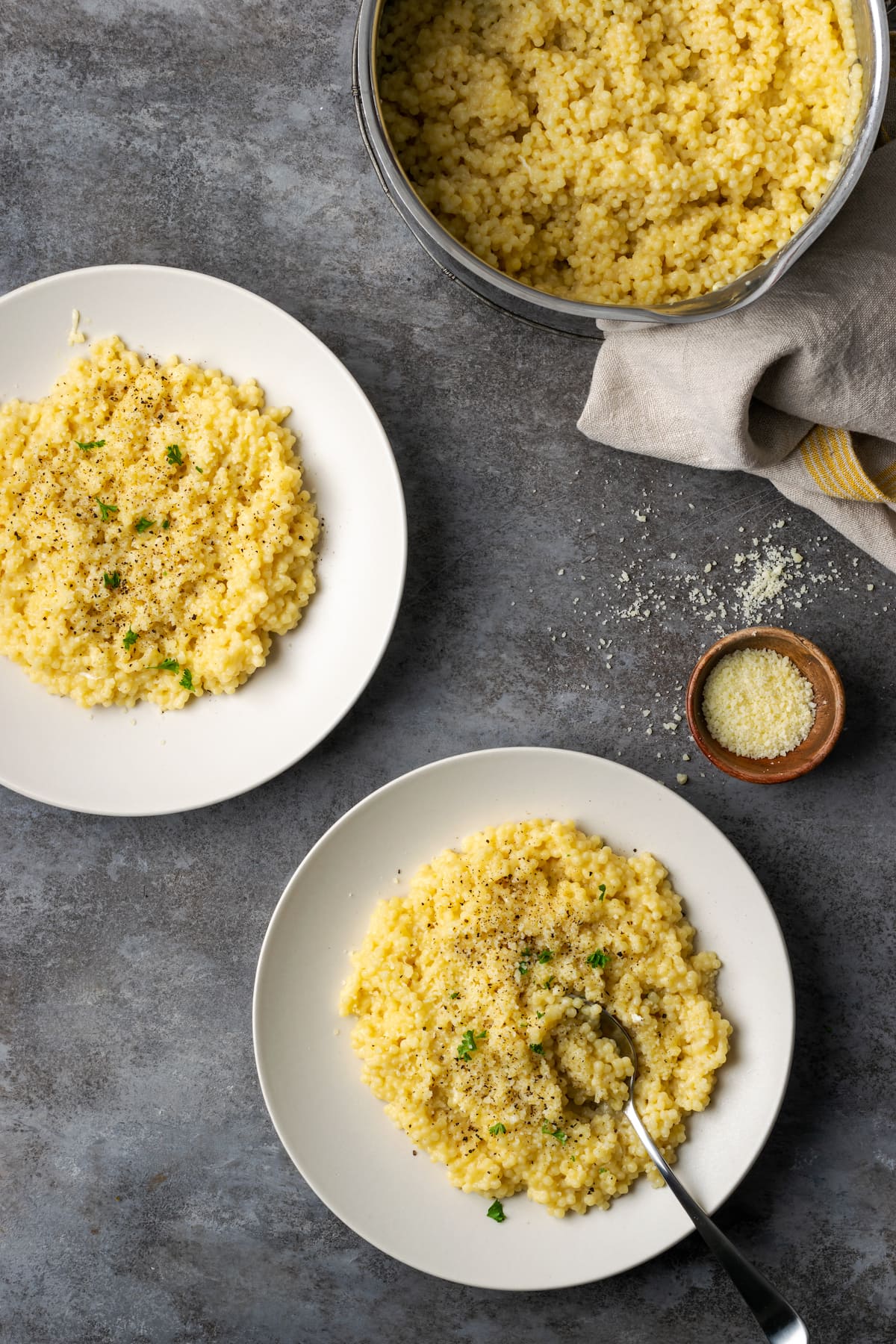 Dos porciones de pastina en platos blancos junto a una olla de pasta pastina.