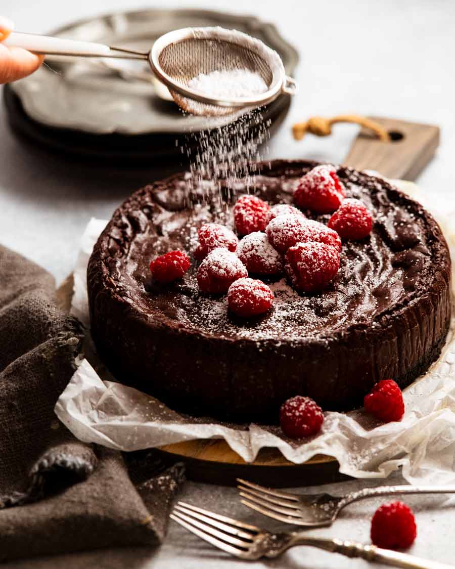Espolvorear un bizcocho de chocolate decorado con frambuesas con azúcar glas