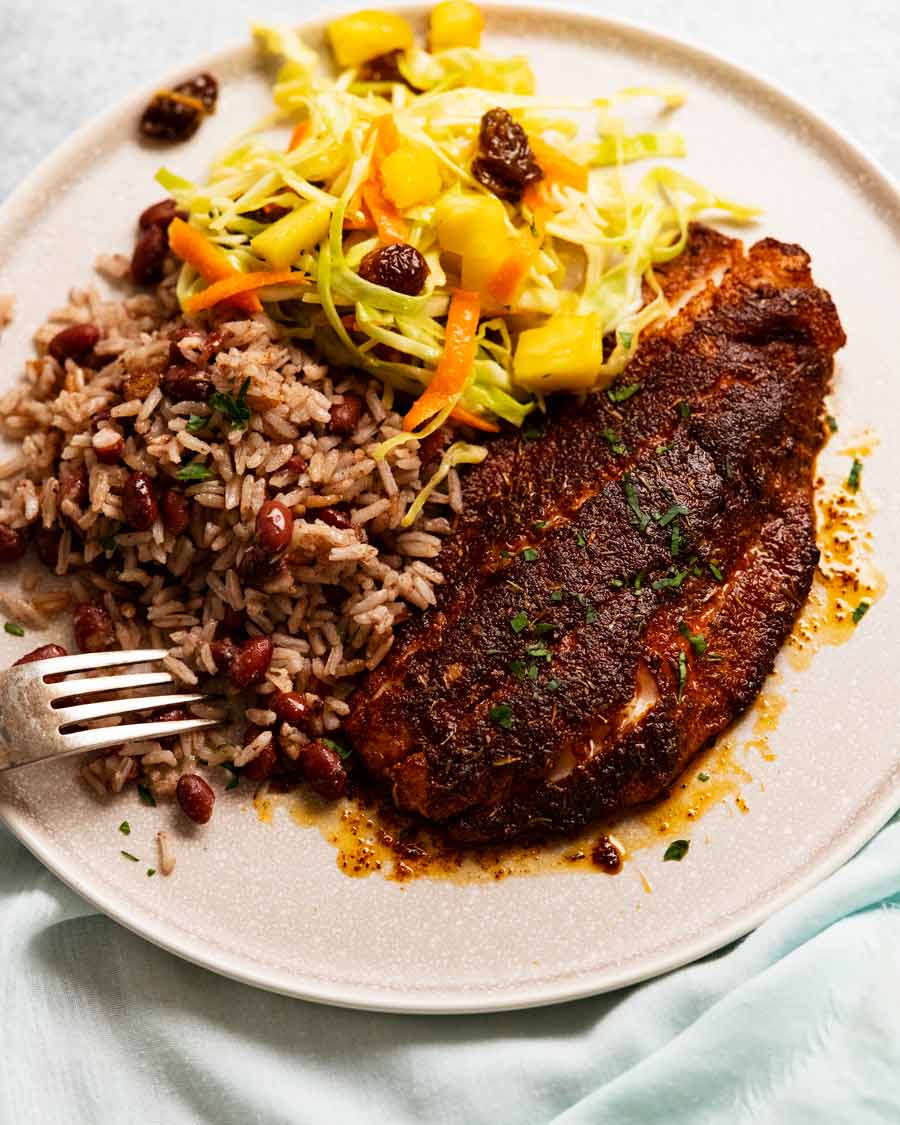 Jerk Fish jamaicano en un plato con ensalada jamaicana y arroz con coco y frijoles