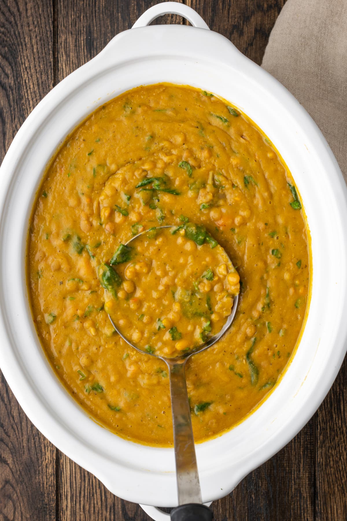 Un cucharón saca una porción de sopa de lentejas de una olla de cocción lenta.
