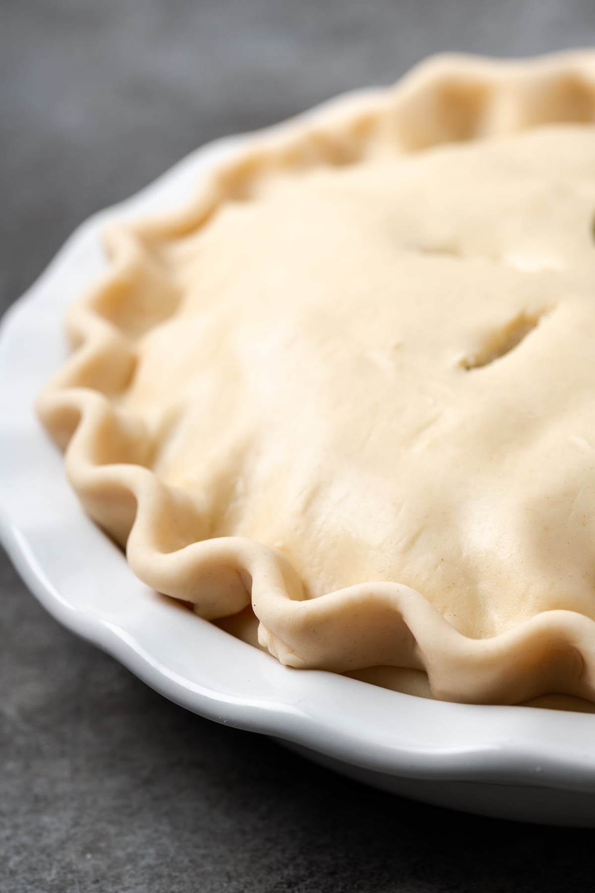 El Chicken Pot Pie casero es la mejor comida reconfortante, hecho con pollo cremoso y verduras horneadas dentro de una masa de pastel de hojaldre mantecosa. Primer plano de pastel de pollo sin hornear dentro de un plato de pastel.