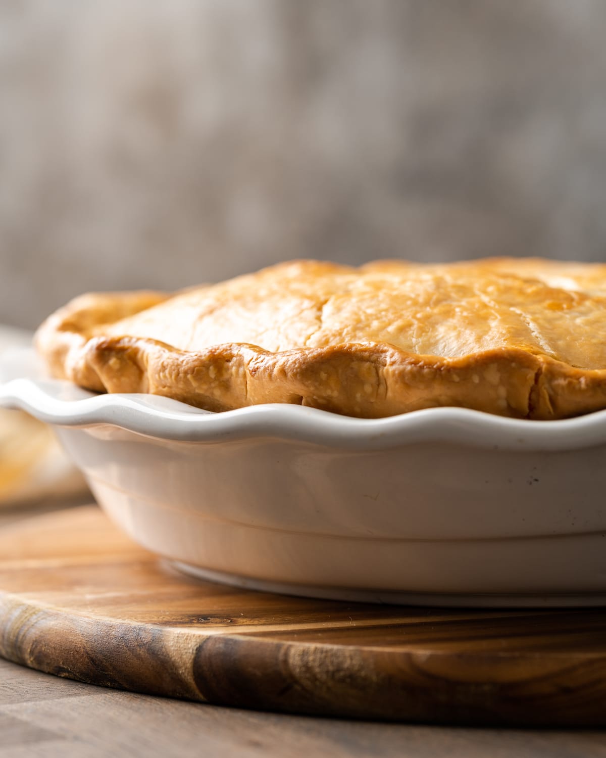 El Chicken Pot Pie casero es la mejor comida reconfortante, hecho con pollo cremoso y verduras horneadas dentro de una masa de pastel de hojaldre mantecosa. Vista lateral de un pastel de pollo al horno en un plato para pastel.