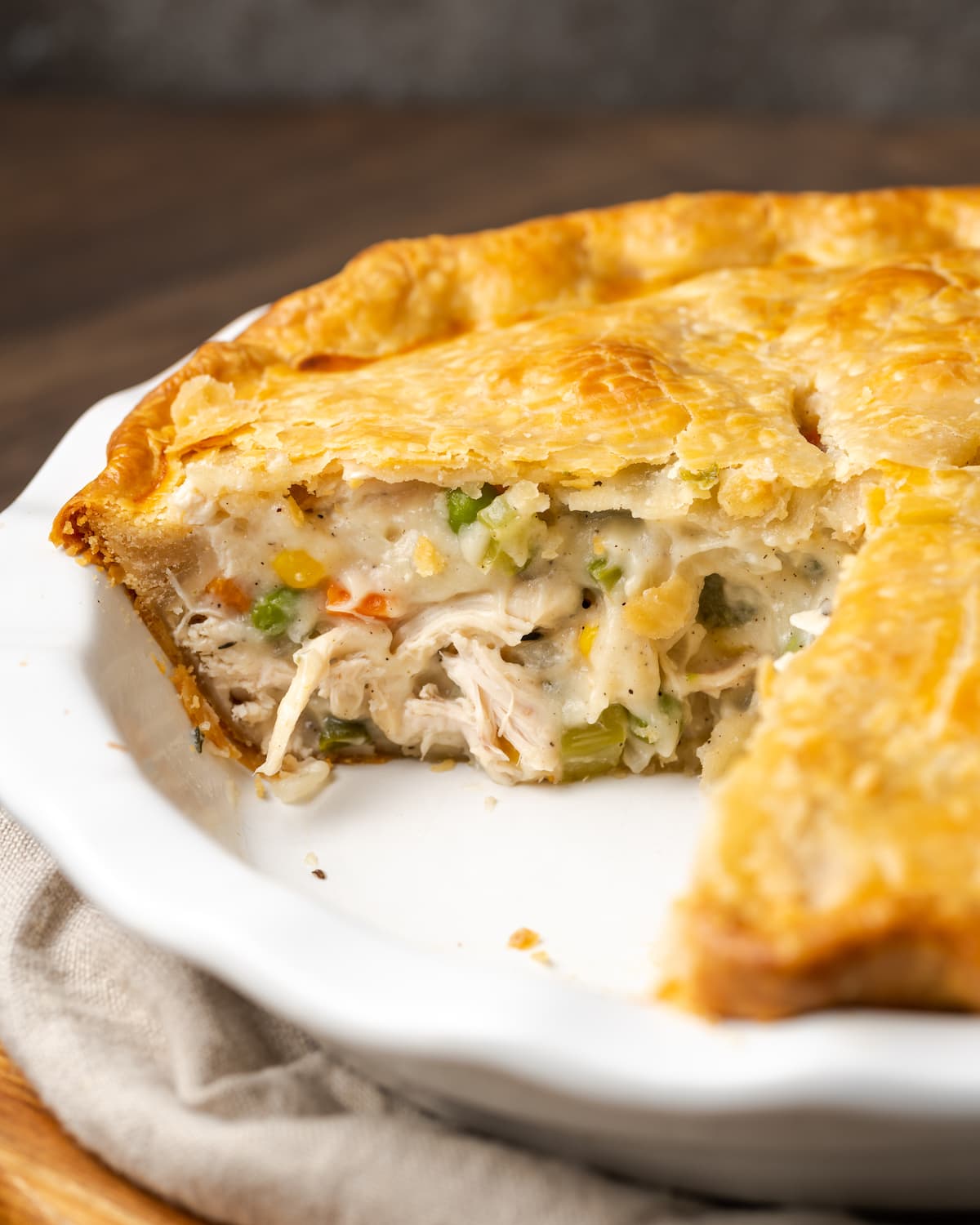 El Chicken Pot Pie casero es la mejor comida reconfortante, hecho con pollo cremoso y verduras horneadas dentro de una masa de pastel de hojaldre mantecosa. Pastel de pollo en un plato para pastel al que le falta una rebanada.