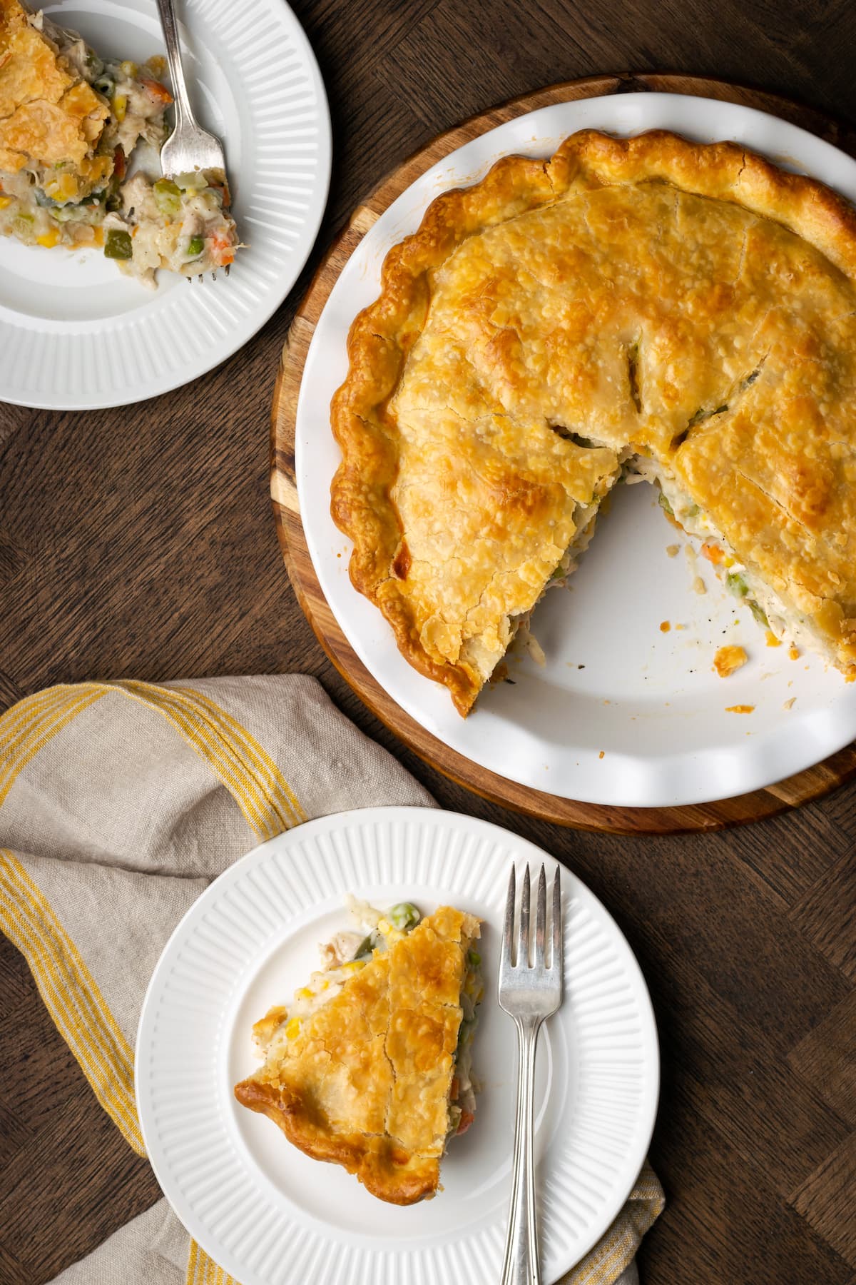El Chicken Pot Pie casero es la mejor comida reconfortante, hecho con pollo cremoso y verduras horneadas dentro de una masa de pastel de hojaldre mantecosa. Vista aérea de un pastel de pollo al que le faltan rebanadas, servido en dos platos cercanos.