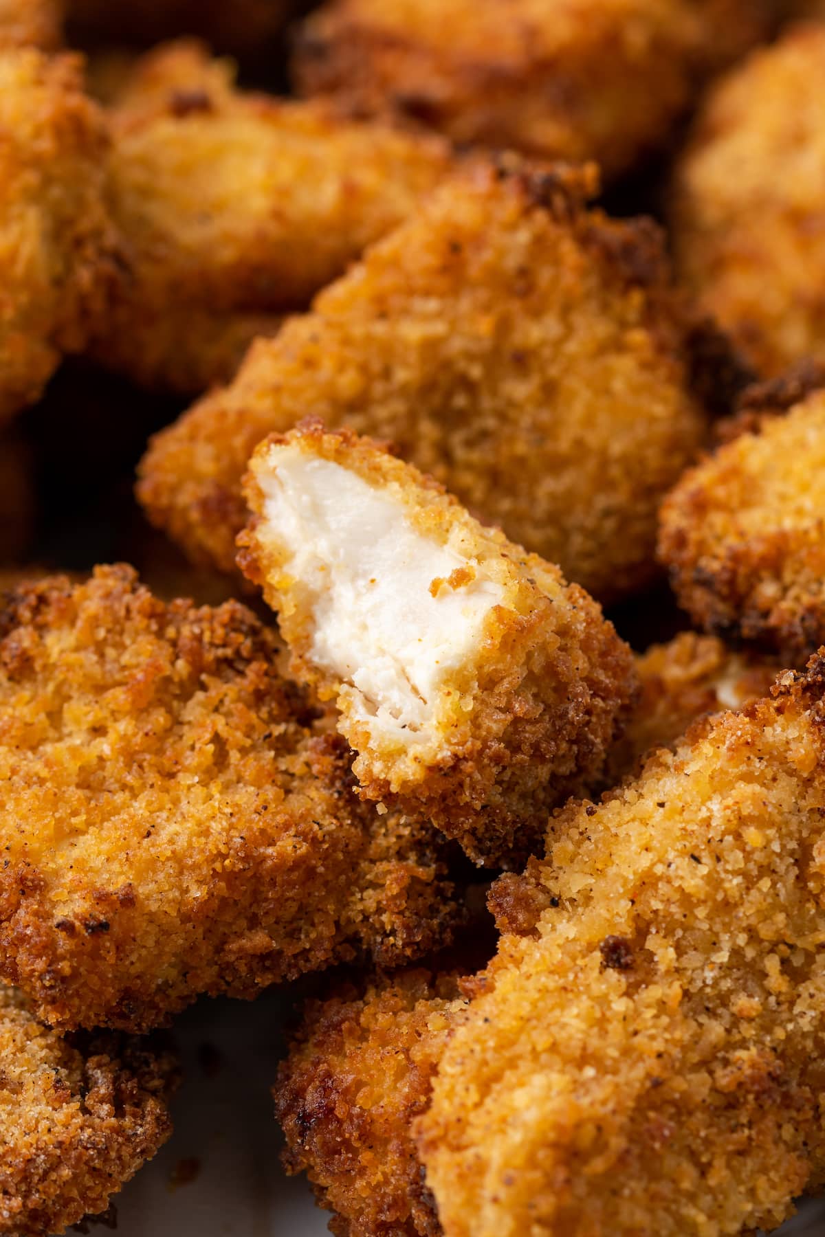 Crispy Air Fryer Popcorn Chicken es irresistiblemente crujiente por fuera y jugoso por dentro, ¡listo en 20 minutos de principio a fin! Primer plano de pollo con palomitas de maíz de la freidora al que le falta un bocado en una pepita.