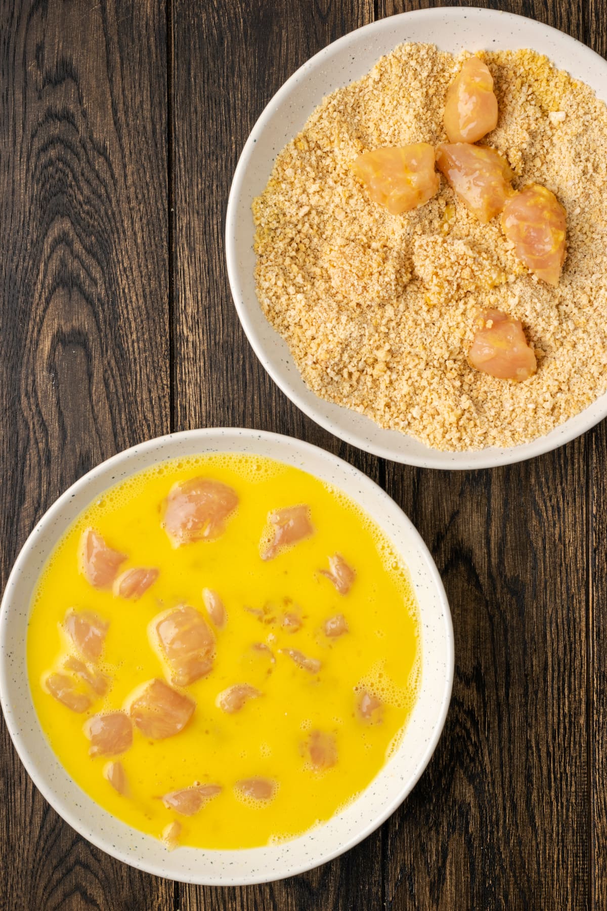 Crispy Air Fryer Popcorn Chicken es irresistiblemente crujiente por fuera y jugoso por dentro, ¡listo en 20 minutos de principio a fin! Trozos de pollo en un huevo lavado junto a otro plato con pollo rebozado en pan rallado.