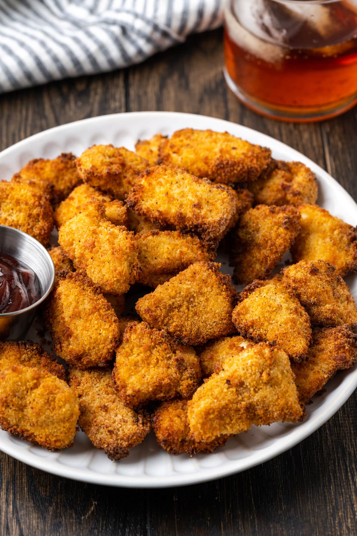 Crispy Air Fryer Popcorn Chicken es irresistiblemente crujiente por fuera y jugoso por dentro, ¡listo en 20 minutos de principio a fin! Pollo crujiente con palomitas de maíz en una freidora en un lugar blanco junto a un ramekin de salsa BBQ para mojar.