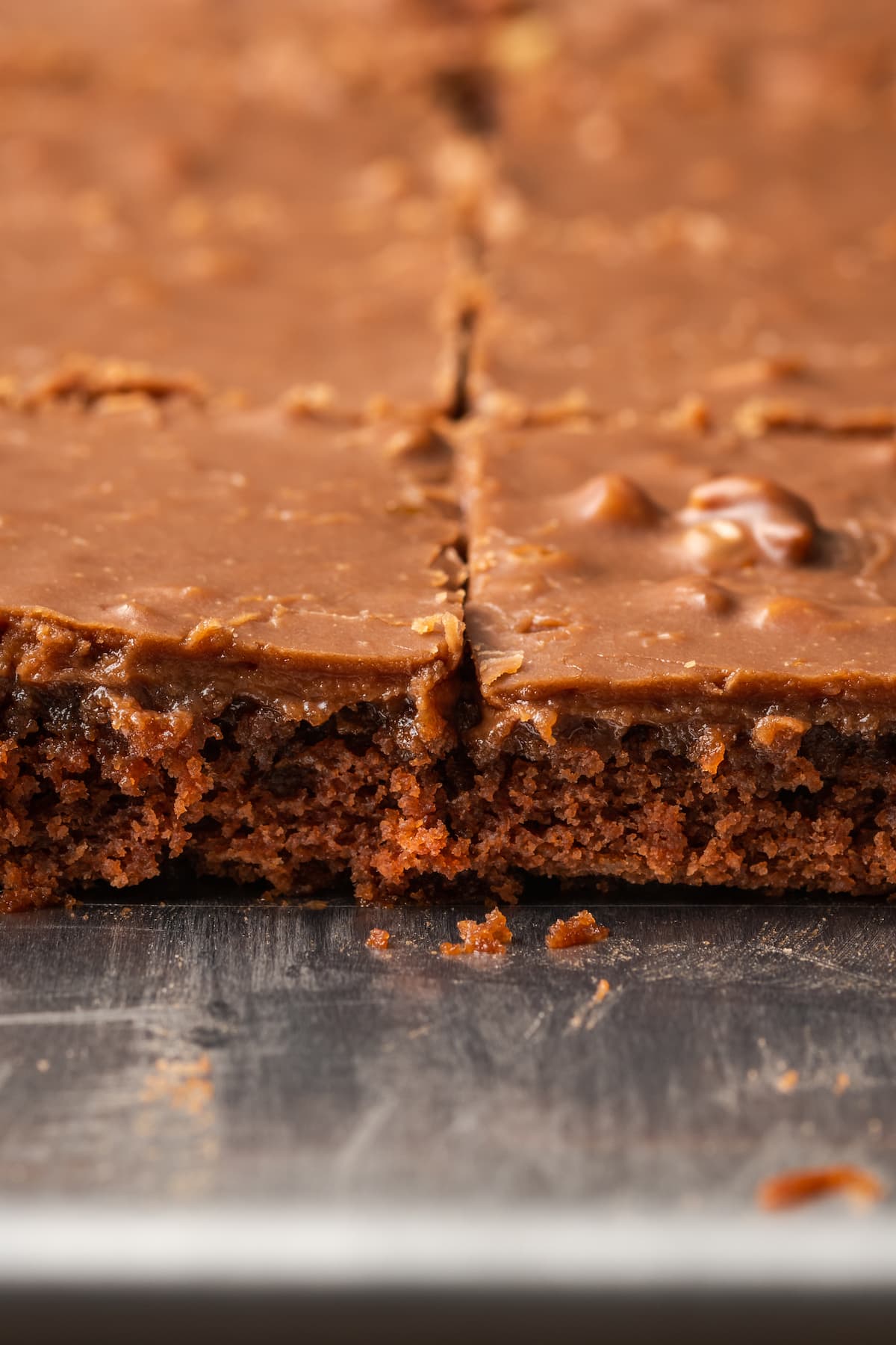 Fudgy Texas Sheet Cake es el sueño de los amantes de los pasteles de chocolate. Esta receta fácil de pastel está cubierta con glaseado de chocolate y es perfecta para fiestas. Primer plano de rebanadas de pastel de hoja de chocolate de Texas en una bandeja de hoja.