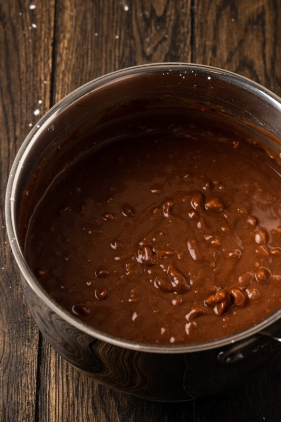 Fudgy Texas Sheet Cake es el sueño de los amantes de los pasteles de chocolate. Esta receta fácil de pastel está cubierta con glaseado de chocolate y es perfecta para fiestas. Glaseado de chocolate con nueces en una cacerola.