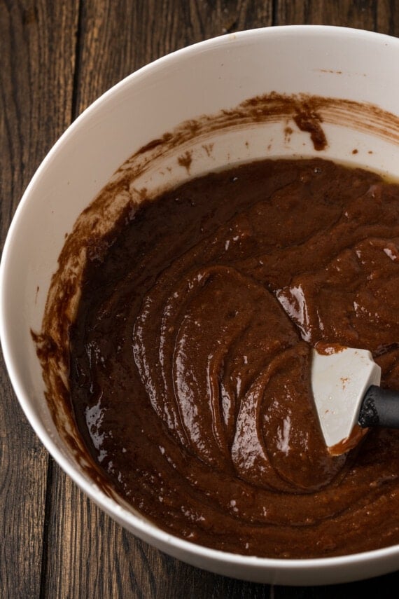 Fudgy Texas Sheet Cake es el sueño de los amantes de los pasteles de chocolate. Esta receta fácil de pastel está cubierta con glaseado de chocolate y es perfecta para fiestas. Masa de pastel de chocolate en un tazón grande con una espátula de goma.