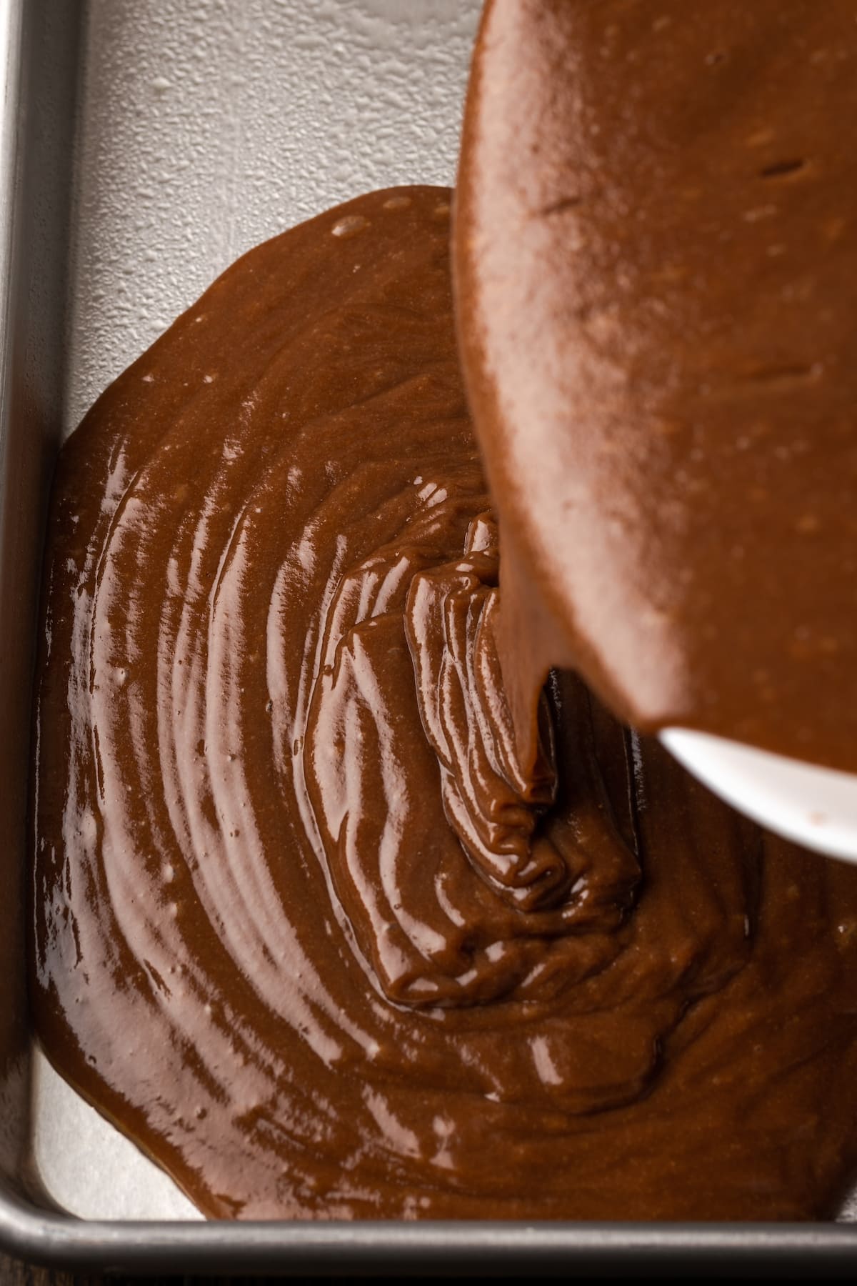 Fudgy Texas Sheet Cake es el sueño de los amantes de los pasteles de chocolate. Esta receta fácil de pastel está cubierta con glaseado de chocolate y es perfecta para fiestas. La masa de pastel de chocolate se vierte en una bandeja para hornear.