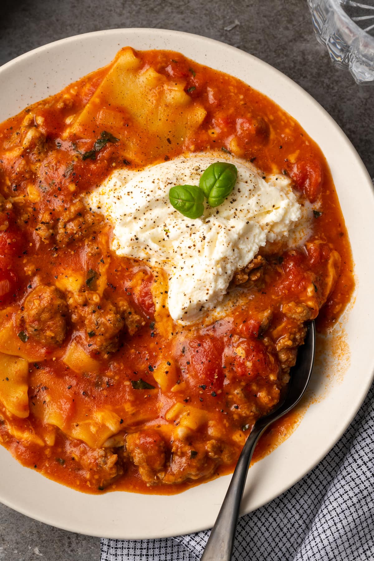 La sopa de lasaña es todo lo que amamos de lasaña casera envuelta en una comida de una sola olla. ¡Prepara esta receta fácil de sopa en 30 minutos o menos! Vista aérea de un tazón de sopa de lasaña cubierto con queso ricotta y hojas de albahaca.