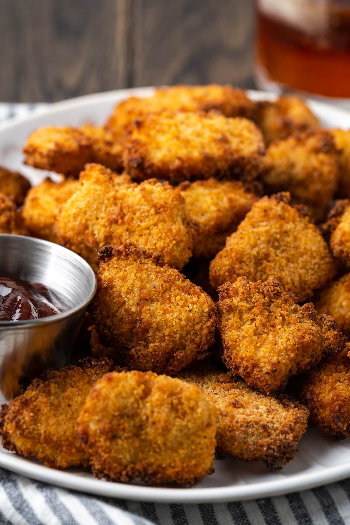 Crispy Air Fryer Popcorn Chicken es irresistiblemente crujiente por fuera y jugoso por dentro, ¡listo en 20 minutos de principio a fin! Pollo crujiente con palomitas de maíz en una freidora en un lugar blanco junto a un ramekin de salsa BBQ para mojar.