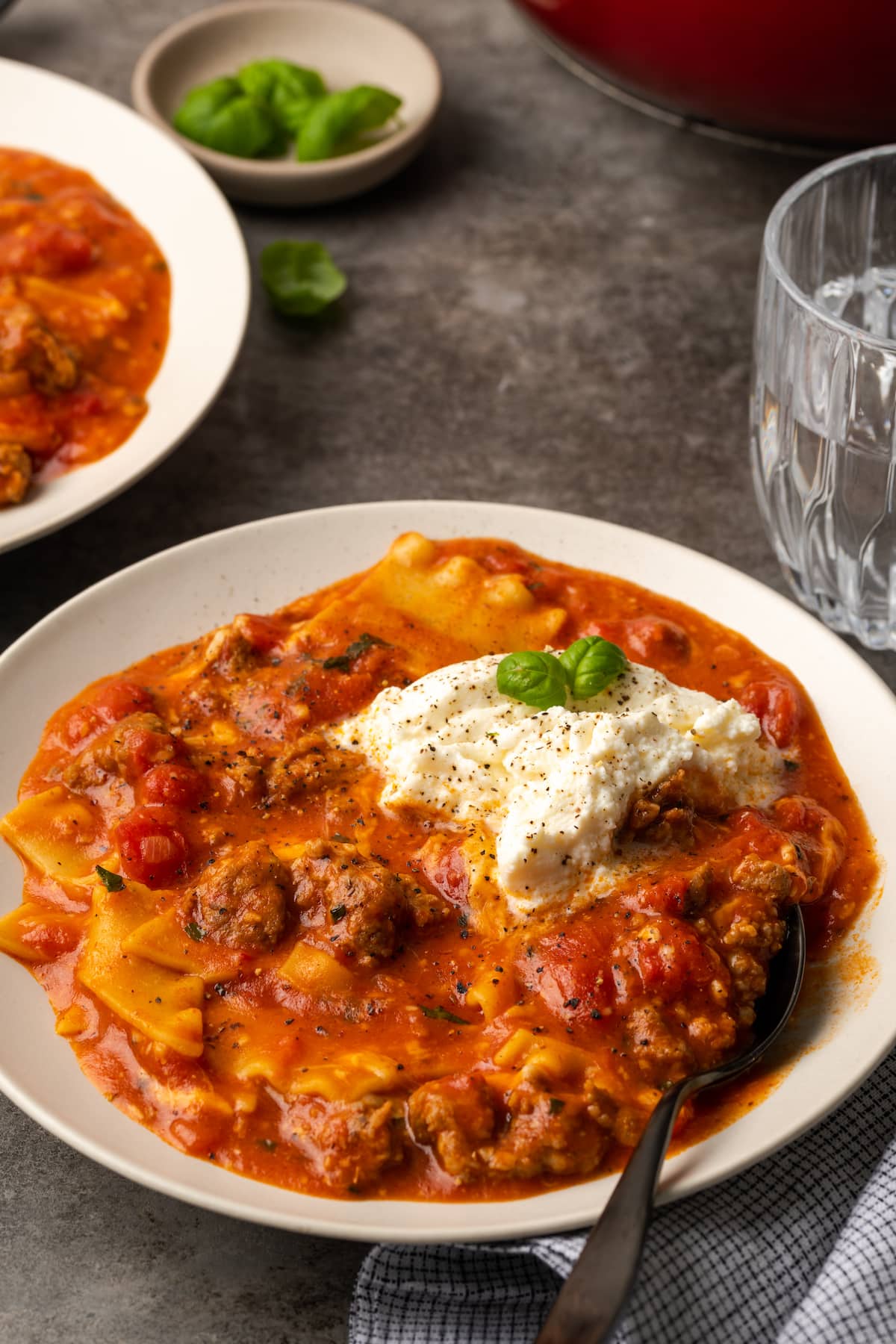 La sopa de lasaña es todo lo que amamos de lasaña casera envuelta en una comida de una sola olla. ¡Prepara esta receta fácil de sopa en 30 minutos o menos! Un tazón de sopa de lasaña cubierto con queso ricotta y hojas de albahaca.
