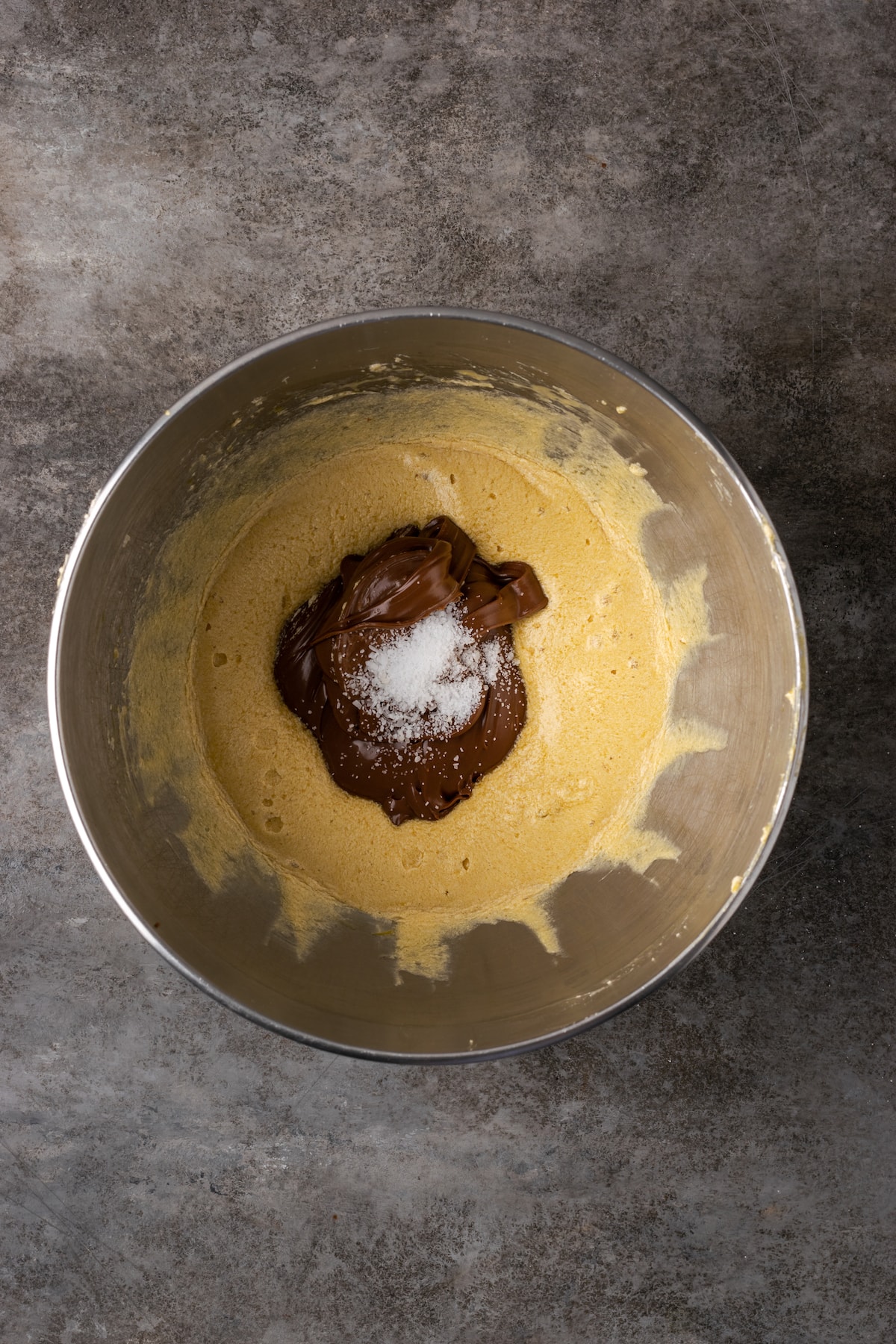 Los brownies caseros de Nutella son ricos, dulces y se arremolinan con crema de chocolate y avellanas. ¡Prepáralos en un tazón con solo 7 ingredientes! Nutella y sal agregadas a los ingredientes del brownie en un tazón para mezclar.