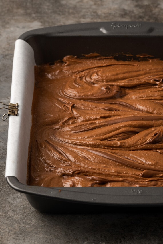 Los brownies caseros de Nutella son ricos, dulces y se arremolinan con crema de chocolate y avellanas. ¡Prepáralos en un tazón con solo 7 ingredientes! Nutella revolvió la masa de brownie en un molde para hornear.