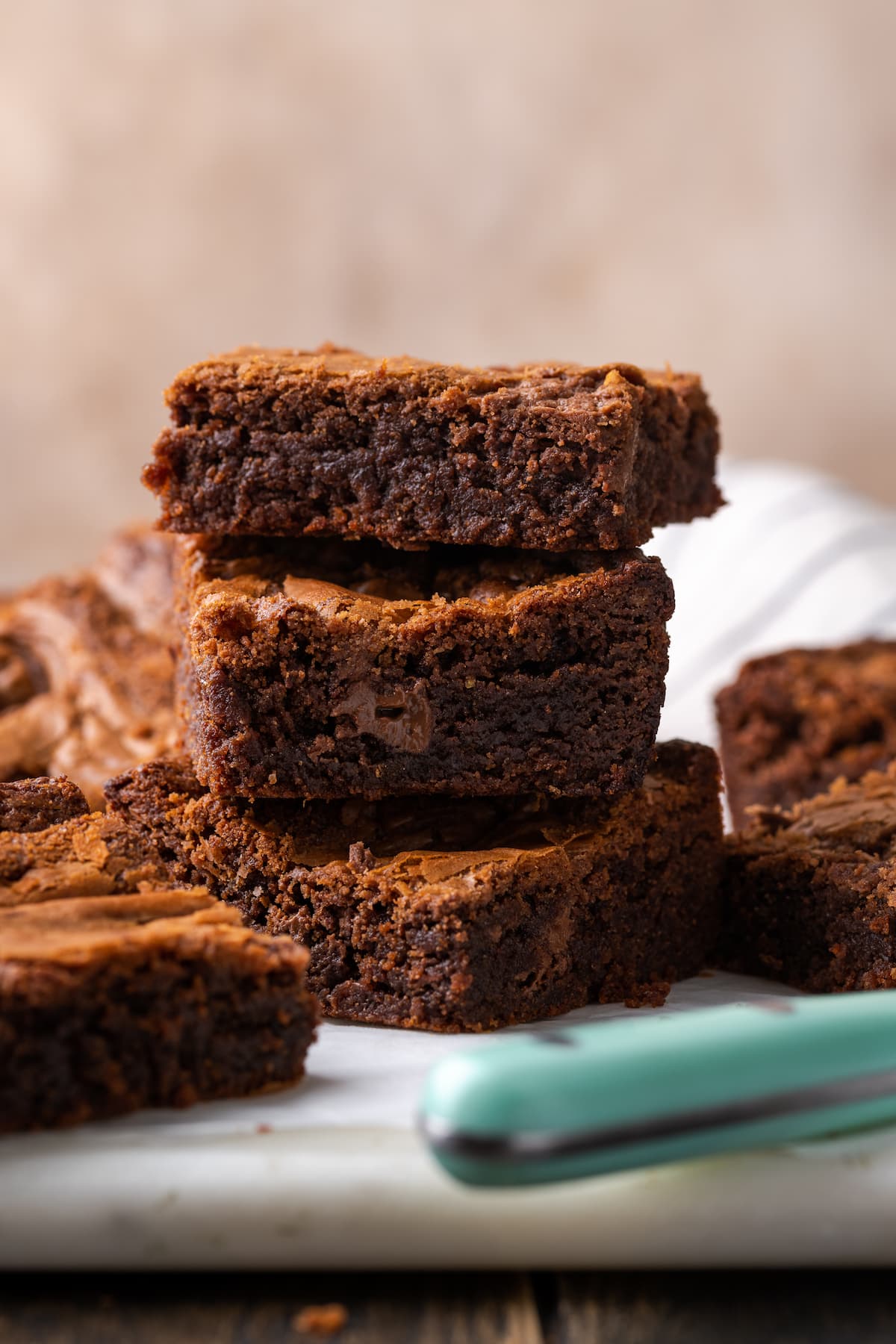 Los brownies caseros de Nutella son ricos, dulces y se arremolinan con crema de chocolate y avellanas. ¡Prepáralos en un tazón con solo 7 ingredientes! Tres brownies de Nutella apilados uno encima del otro en una tabla para cortar, rodeados de más Brownies.