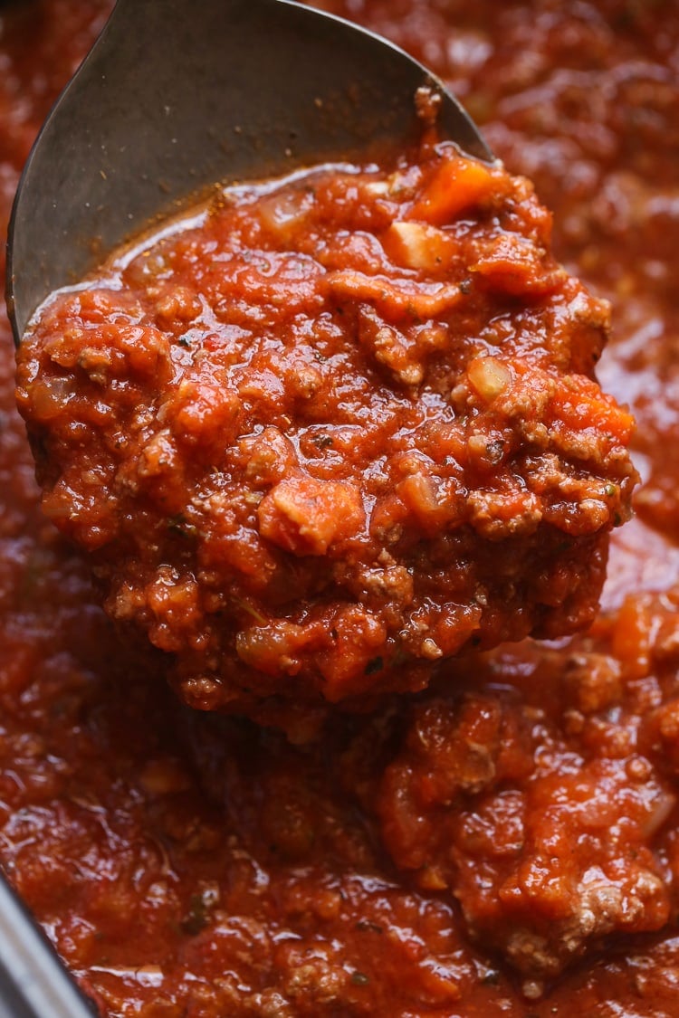 Una cuchara levanta la salsa boloñesa de cocción lenta de una olla.