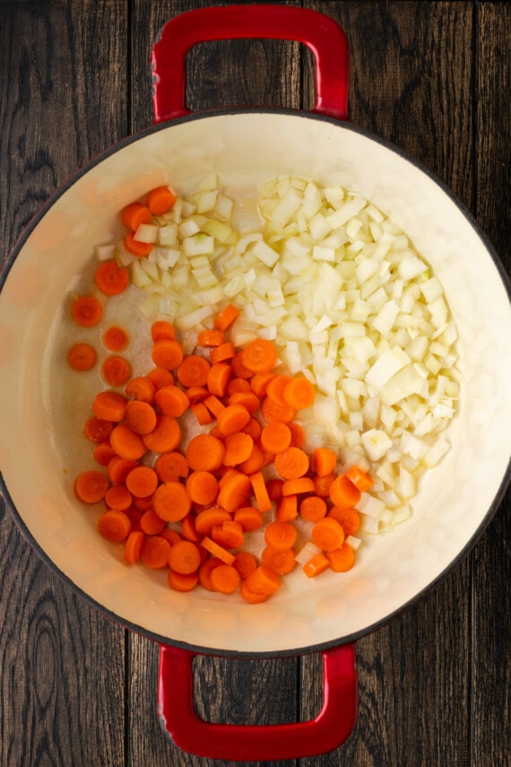 Zanahorias picadas y cebolla en el fondo de un horno holandés grande.