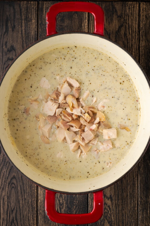 Pollo cocido en cubos agregado a una olla de caldo de sopa cremosa.