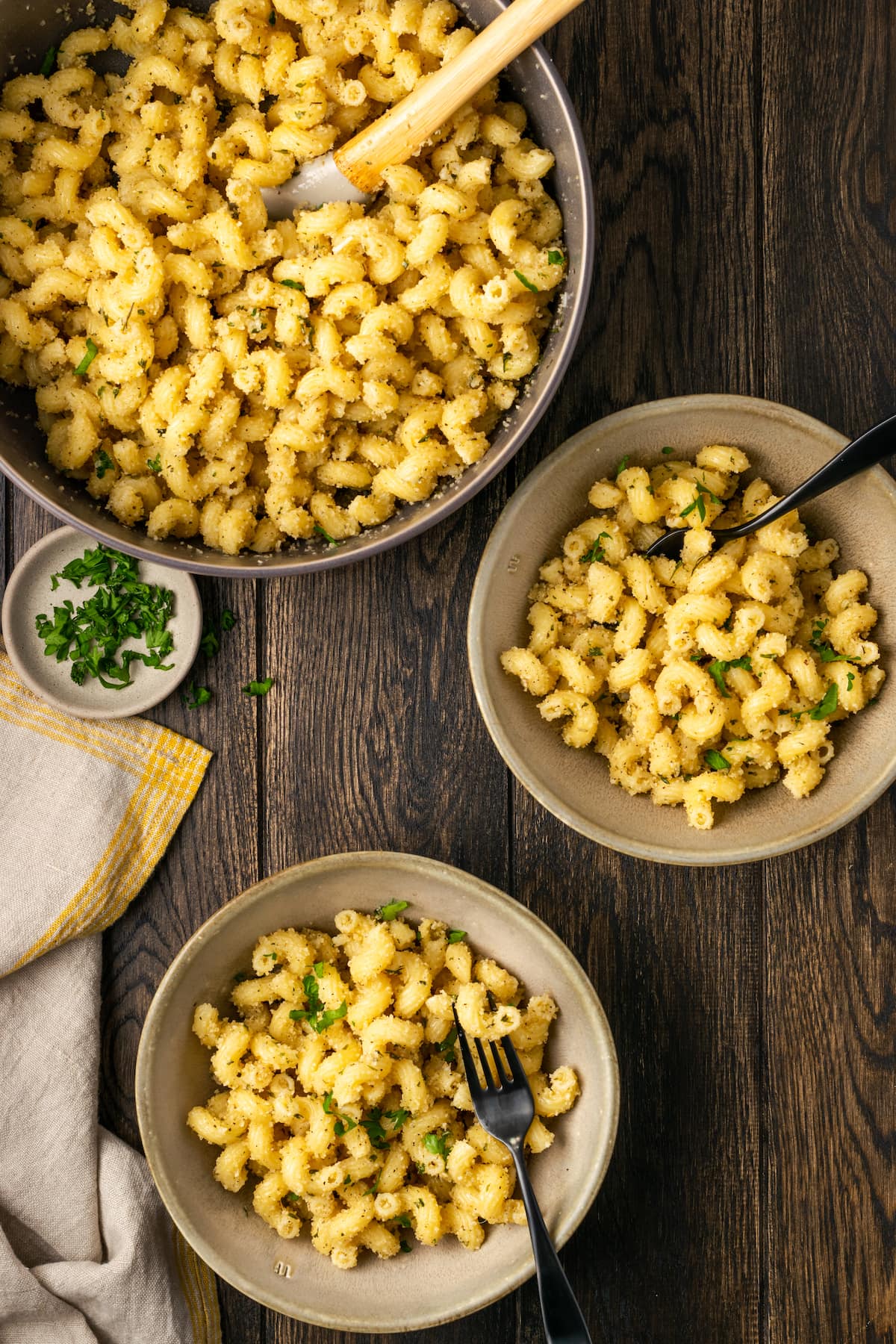 Vista aérea de dos tazones de pasta con pan de ajo junto a un tazón grande de pasta con una cuchara de madera.