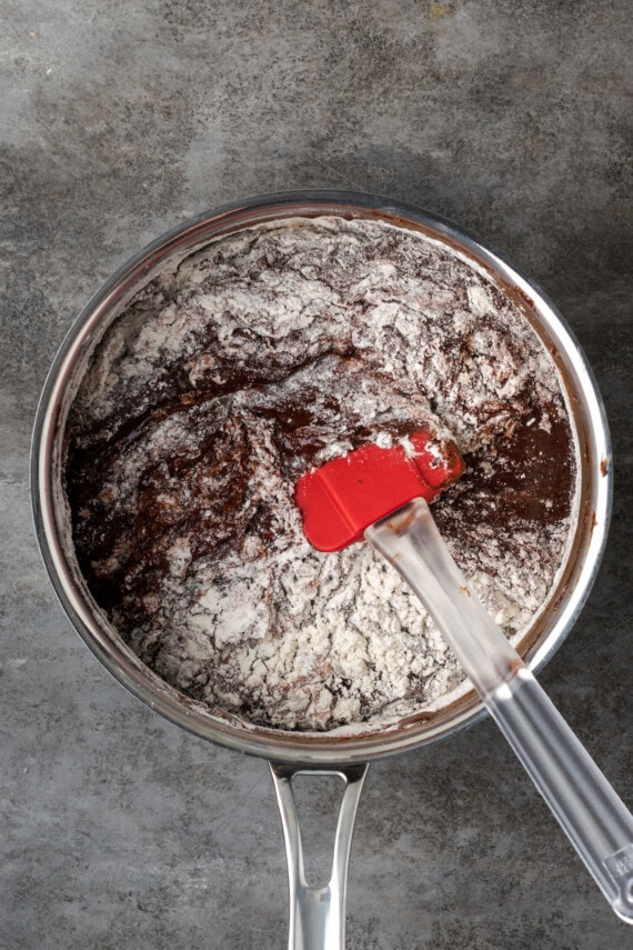 Esta receta fácil de brookies combina brownies de chocolate con galletas masticables con chispas de chocolate. ¡Las galletas de brownie con chocolate son lo mejor de ambos mundos! Harina revuelta en la masa de brownie en una cacerola.