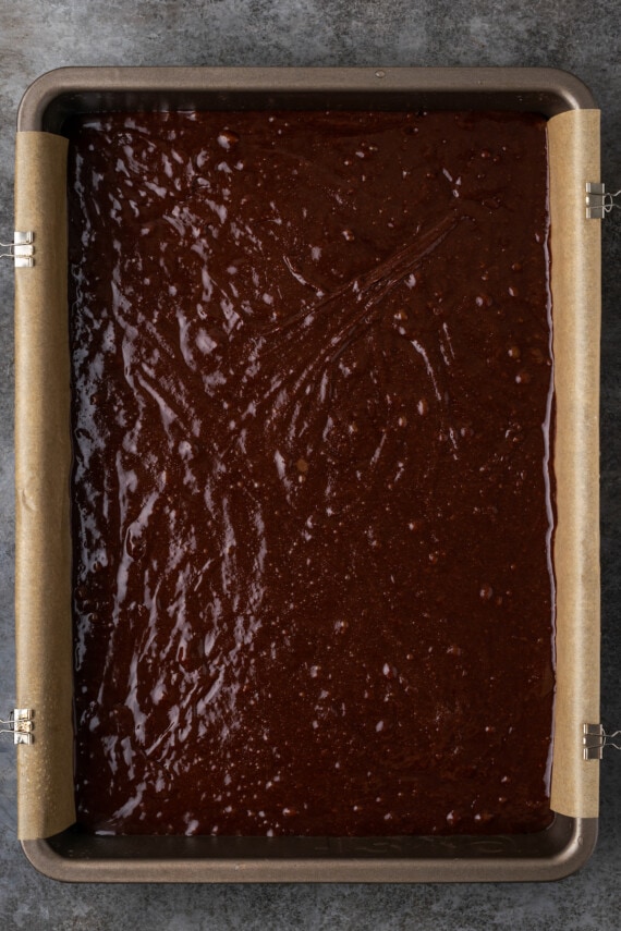 Esta receta fácil de brookies combina brownies de chocolate con galletas masticables con chispas de chocolate. ¡Las galletas de brownie con chocolate son lo mejor de ambos mundos! Masa de brownie en un molde para hornear forrado con pergamino.
