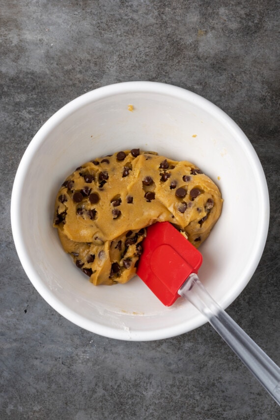 Esta receta fácil de brookies combina brownies de chocolate con galletas masticables con chispas de chocolate. ¡Las galletas de brownie con chocolate son lo mejor de ambos mundos! Las chispas de chocolate se mezclan con la masa para galletas en un tazón blanco.