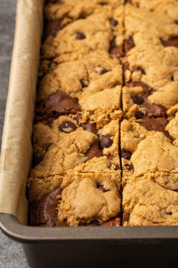 Esta receta fácil de brookies combina brownies de chocolate con galletas masticables con chispas de chocolate. ¡Las galletas de brownie con chocolate son lo mejor de ambos mundos! Cerca de brookies horneados en un molde para hornear forrado de pergamino.