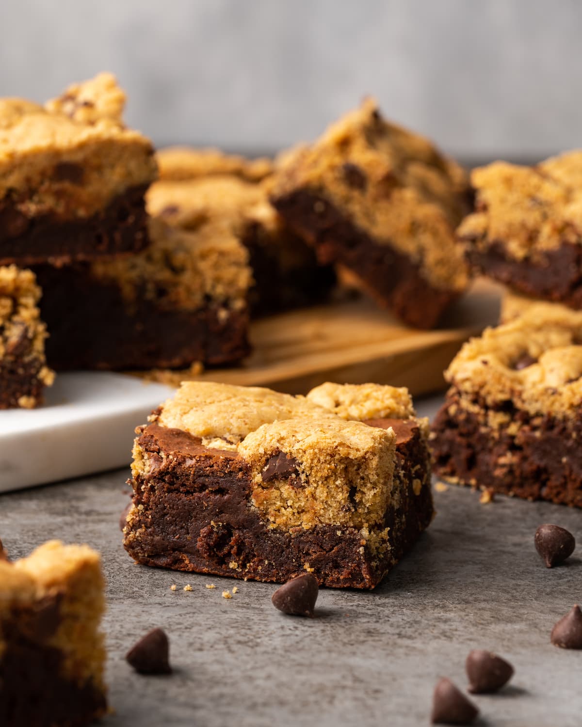 Esta receta fácil de brookies combina brownies de chocolate con galletas masticables con chispas de chocolate. ¡Las galletas de brownie con chocolate son lo mejor de ambos mundos! Brookies surtidos en una encimera con más brookies en el fondo.