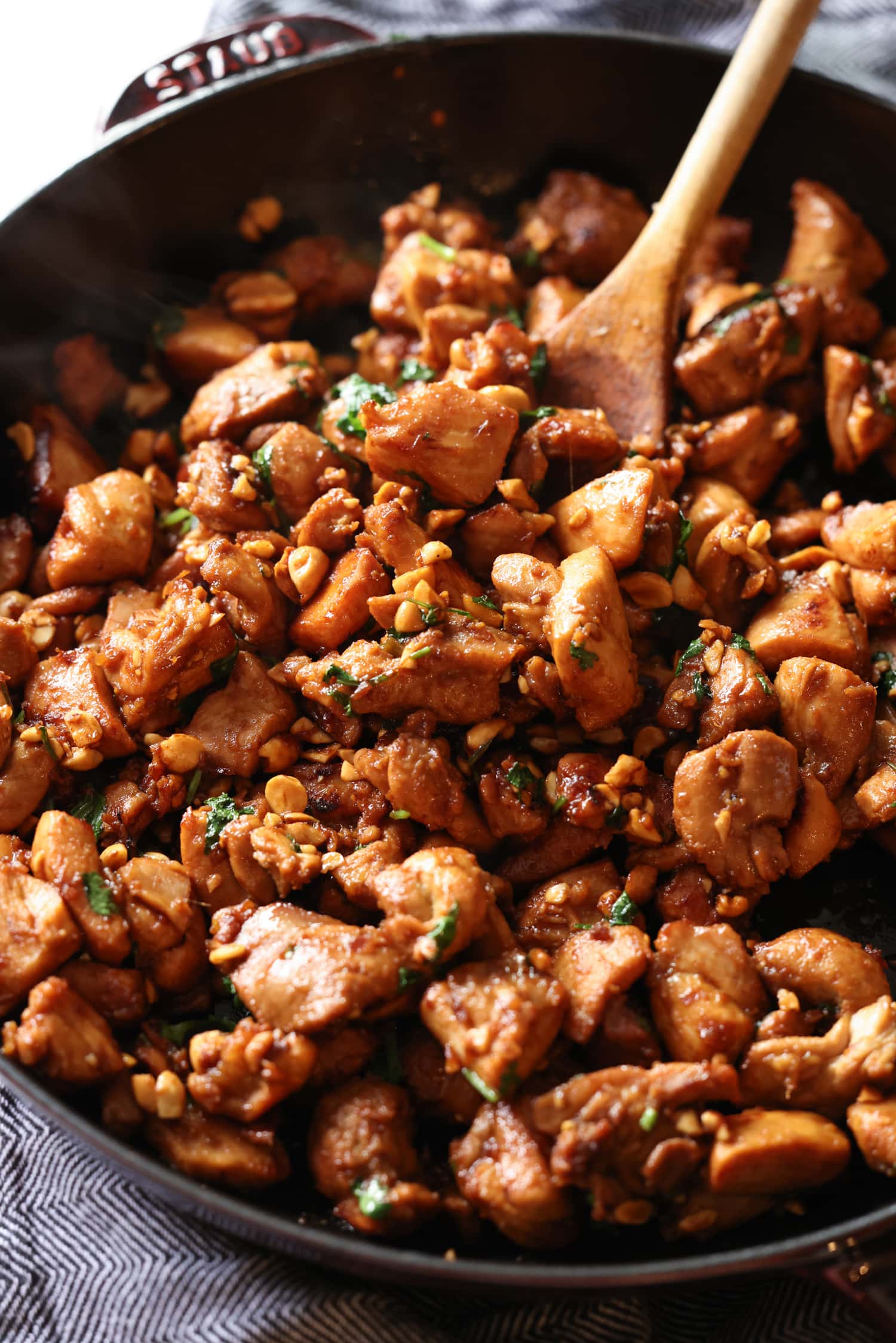 Este sencillo pollo al jengibre está cubierto con un dulce y pegajoso glaseado de soya y jengibre al estilo asiático salpicado de maní. ¡Listo en menos de 20 minutos! El pollo al jengibre se revuelve con una cuchara de madera mientras se cocina en una sartén de hierro fundido.