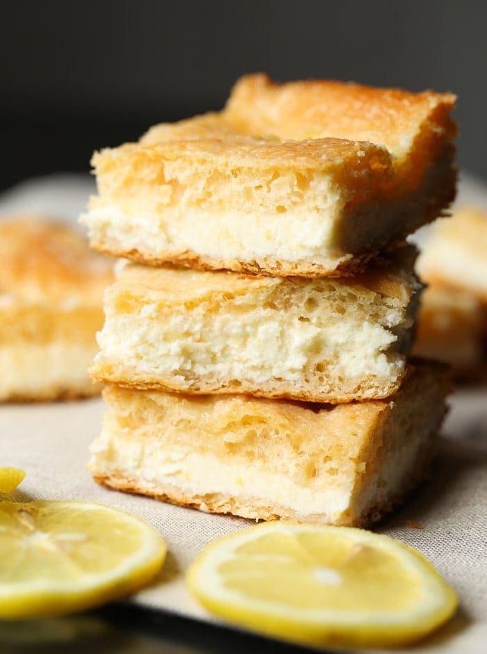 Una pila de tres barras de queso crema de limón rodeadas de rodajas de limón.