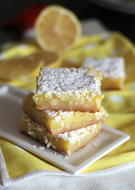 Una pila de tres cuadrados de coco y limón sostenidos en un pequeño plato rectangular.