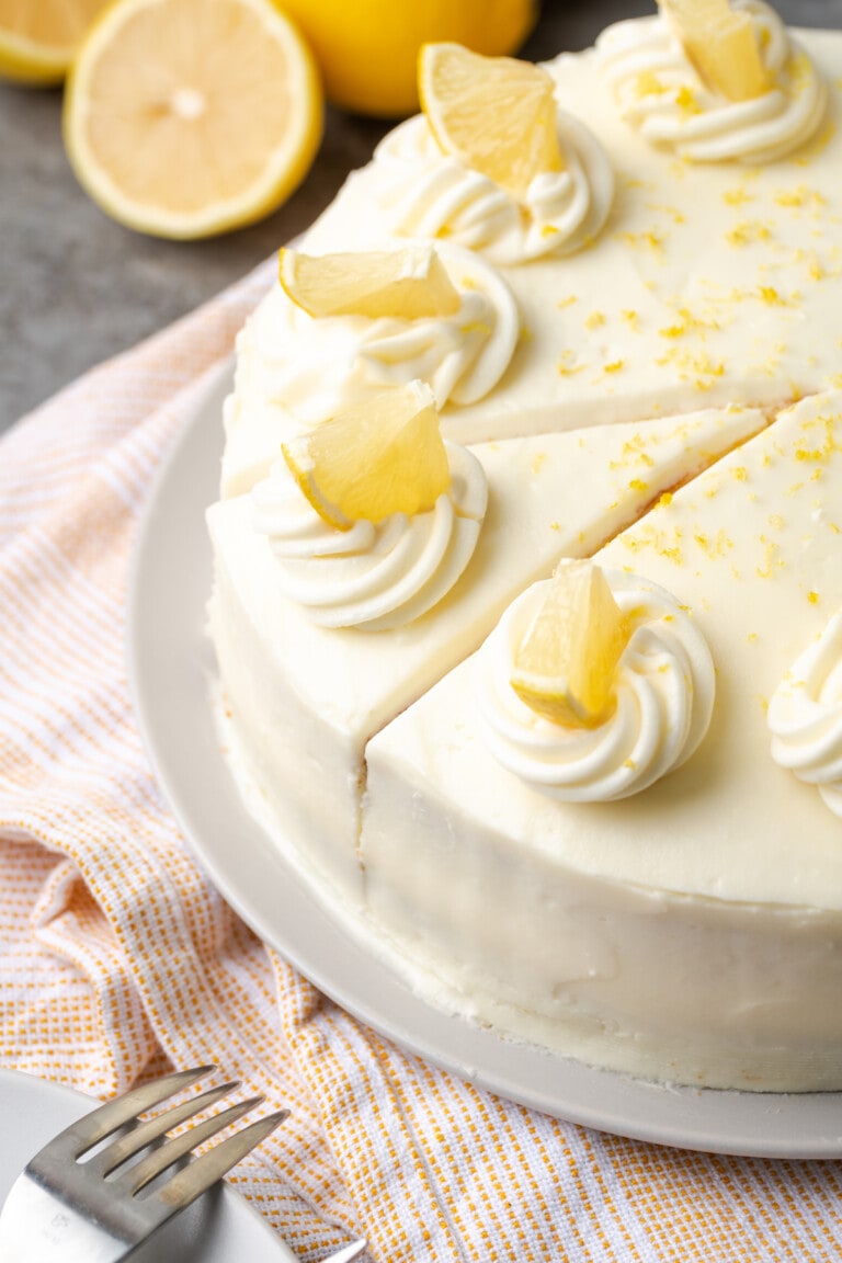 Pastel de limonada cubierto con remolinos de glaseado y rodajas de limón, con una rodaja cortada.