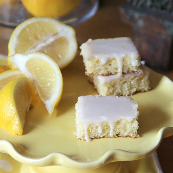Tres brownies de limonada junto a gajos de limón en un plato amarillo.