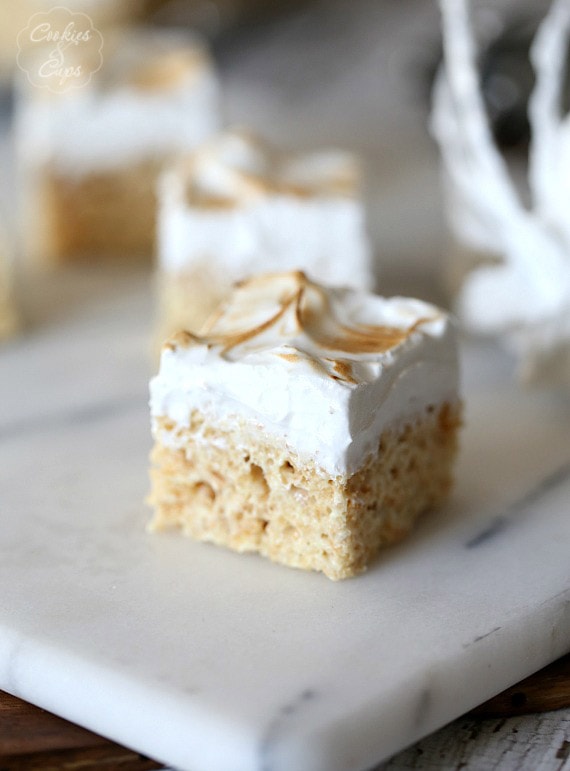Primer plano de una golosina krispie de arroz con merengue de limón sobre una superficie de mármol, con más golosinas krispie en el fondo.