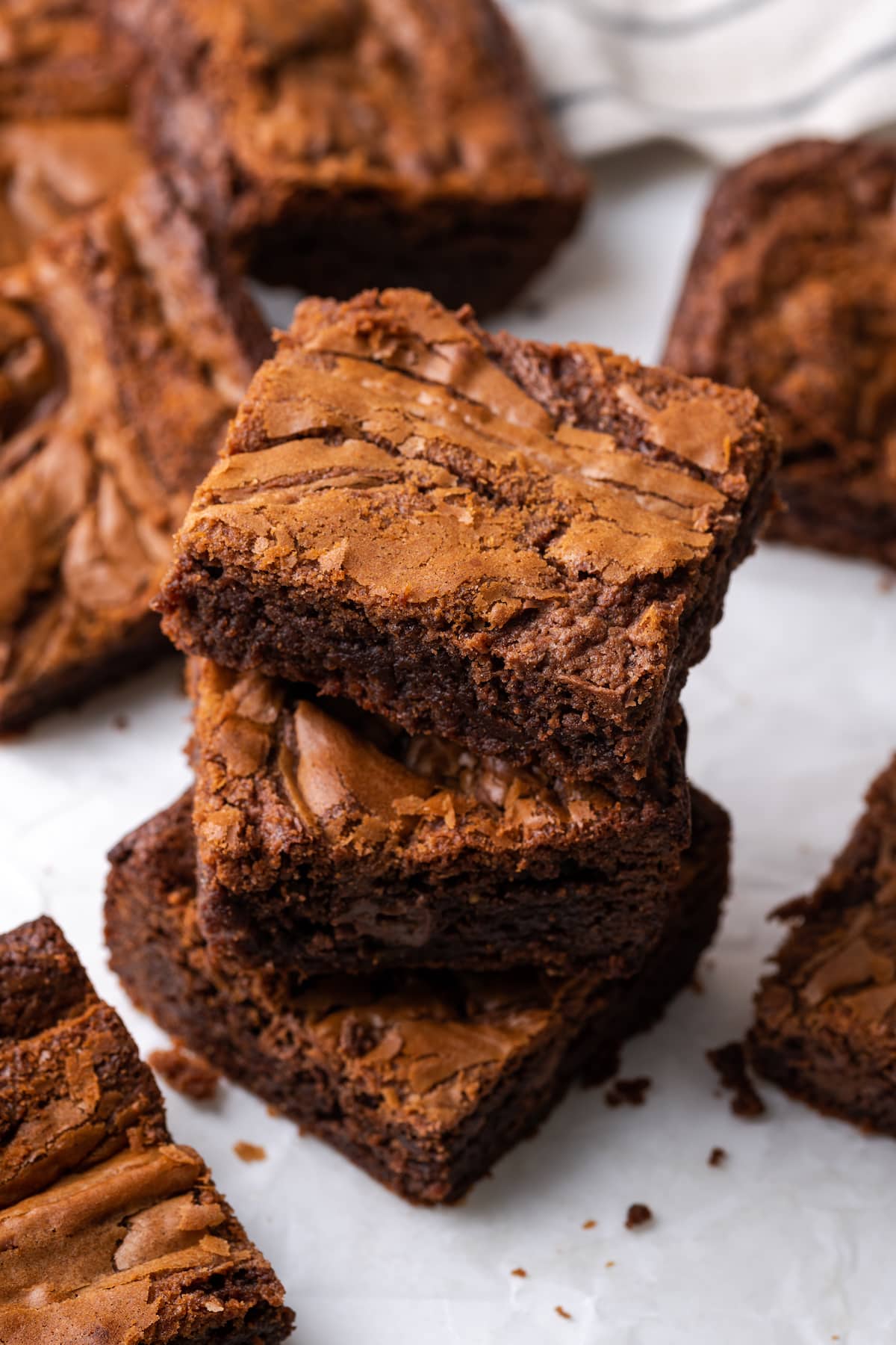 Los brownies caseros de Nutella son ricos, dulces y se arremolinan con crema de chocolate y avellanas. ¡Prepáralos en un tazón con solo 7 ingredientes! Vista aérea de tres brownies de Nutella apilados uno encima de otro en una tabla de cortar, rodeados de más brownies.