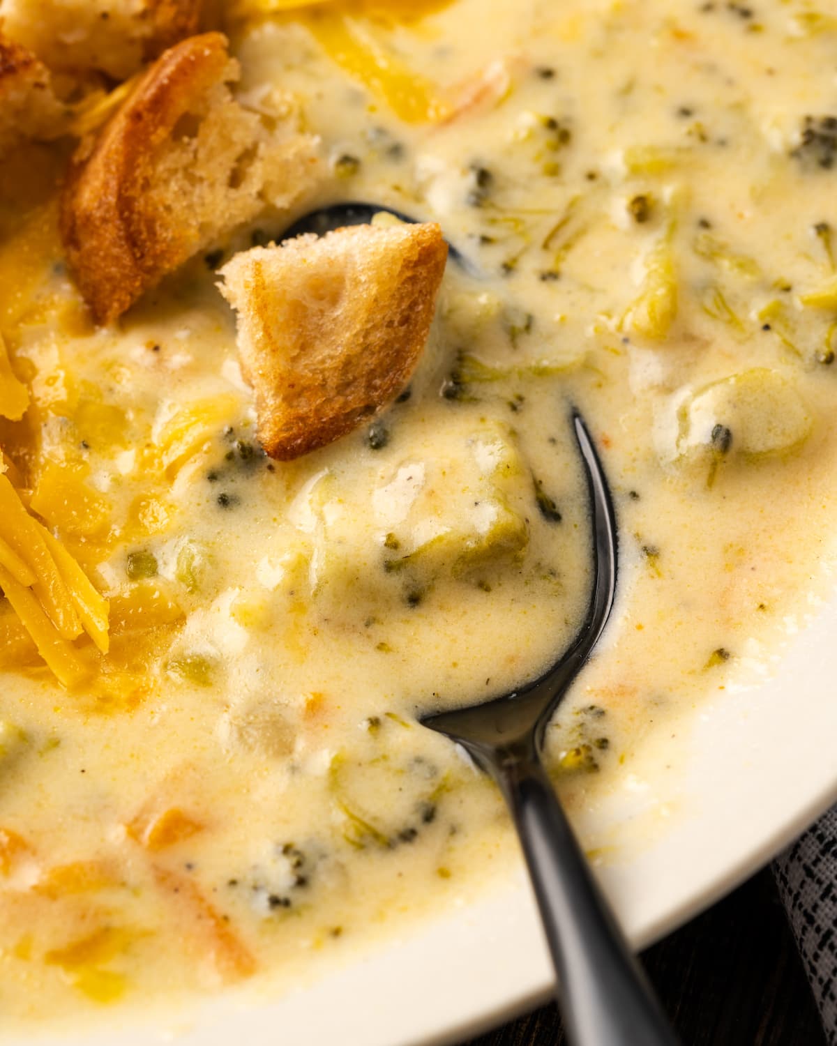 Primer plano de un tazón de sopa instantánea de brócoli y queso cheddar cubierto con picatostes con una cuchara.