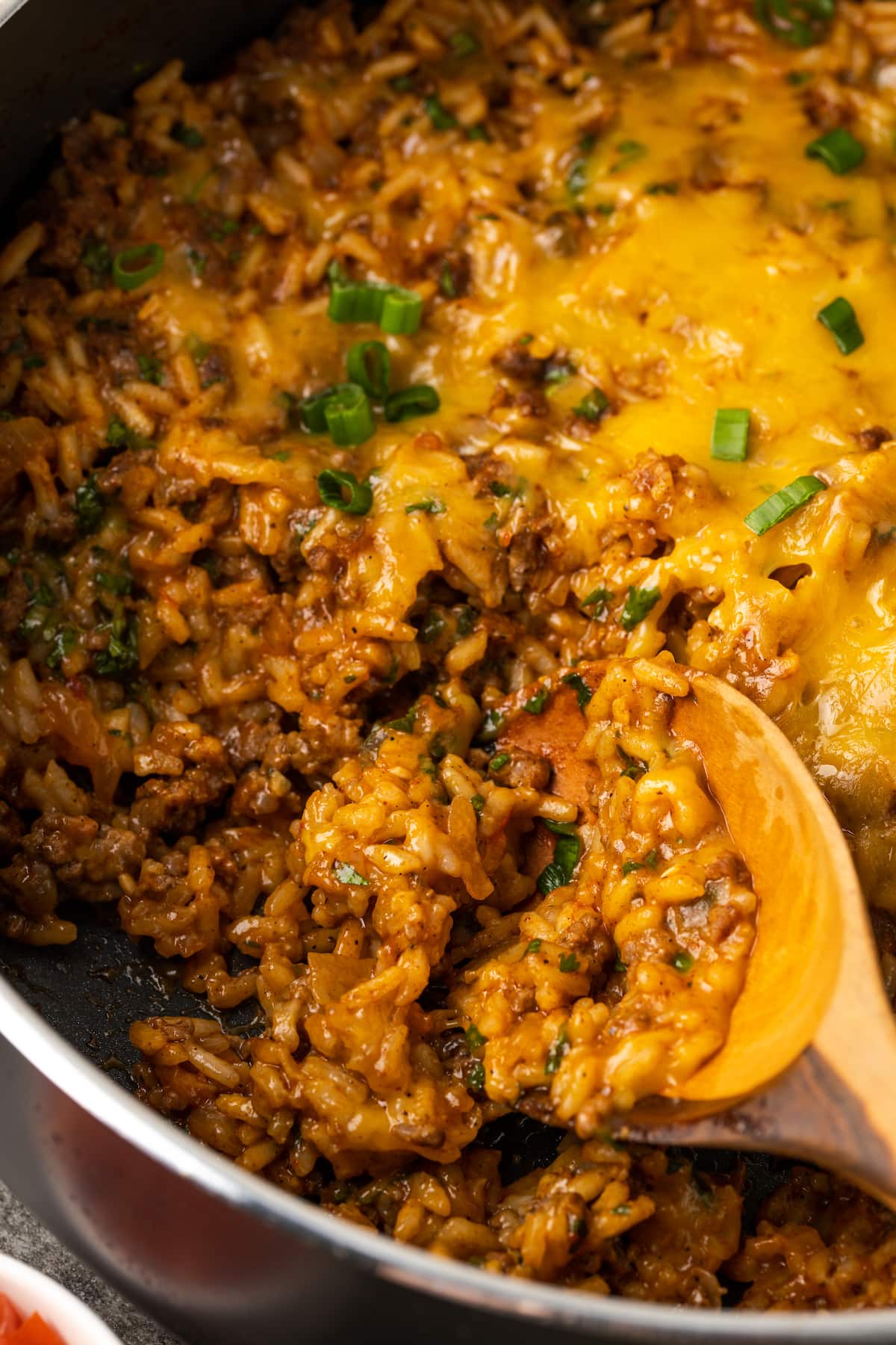 Una cuchara de madera sacando tacos de arroz con queso de una sartén.