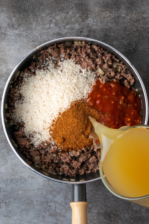 El caldo de pollo se vierte en una sartén con carne molida, arroz, salsa y condimento para tacos.