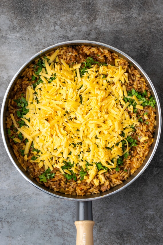 Arroz de taco cocido en una sartén cubierto con cilantro y queso rallado.