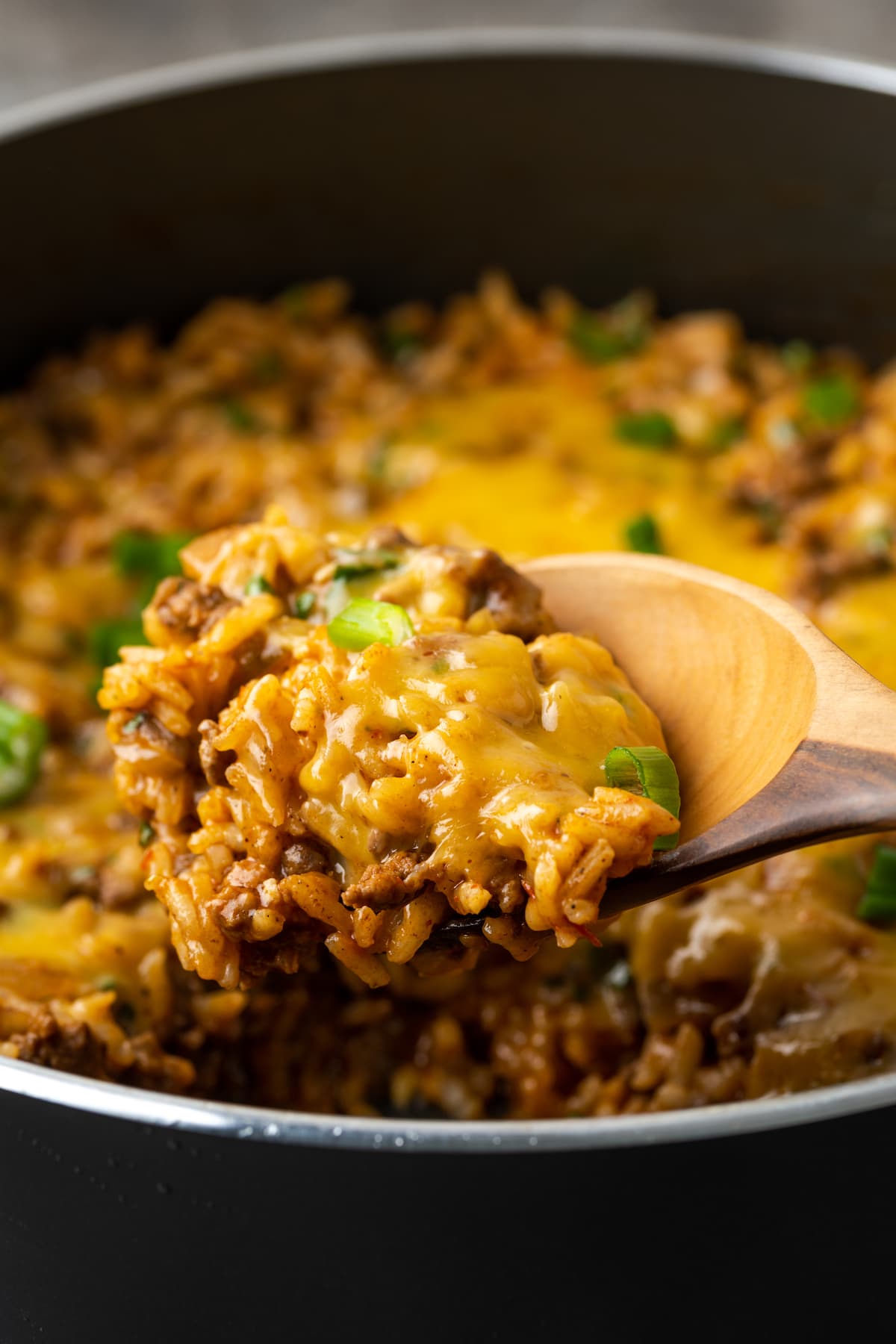 Una cuchara de madera sacando tacos de arroz con queso de una sartén.