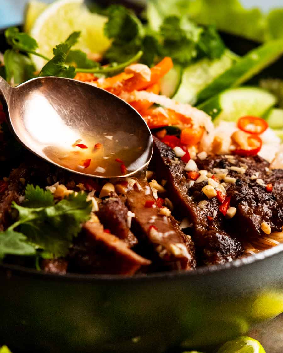 Salsa nuoc cham servida con una cuchara sobre fideos vietnamitas con cerdo al limoncillo (Bún thịt nướng)